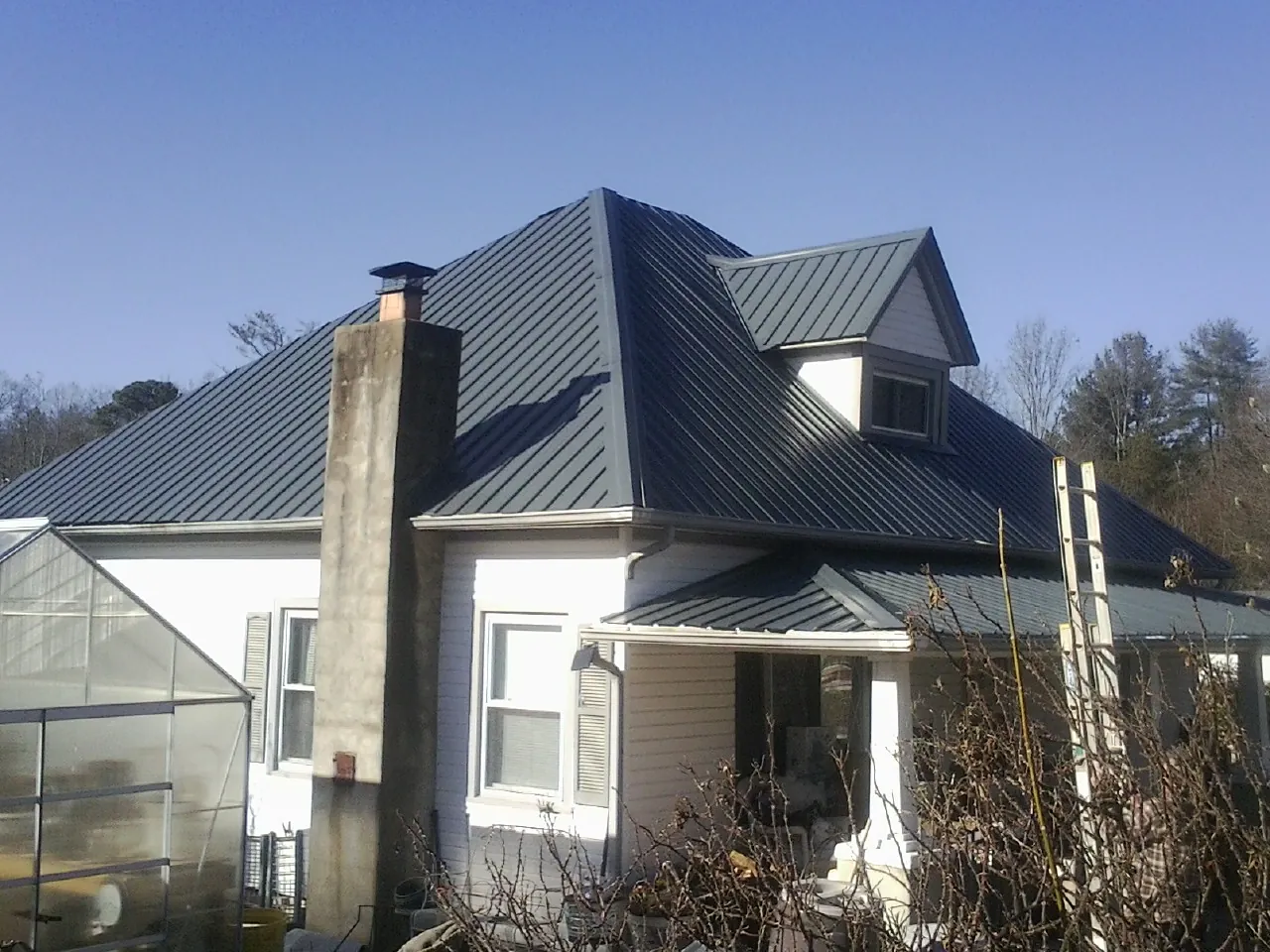 Dark blue standing seam metal roof on a white farmhouse with dormer — Slate & Tile Roof Repair by Roofing Brothers in West Greenwich