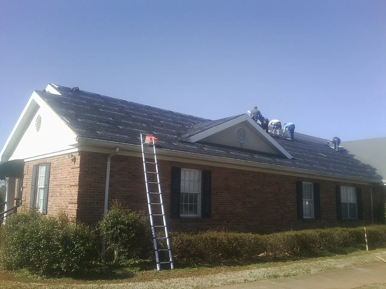 Crew tearing shingles off a brick ranch roof with a ladder set — Metal Roof Repair work by our crew in West Greenwich