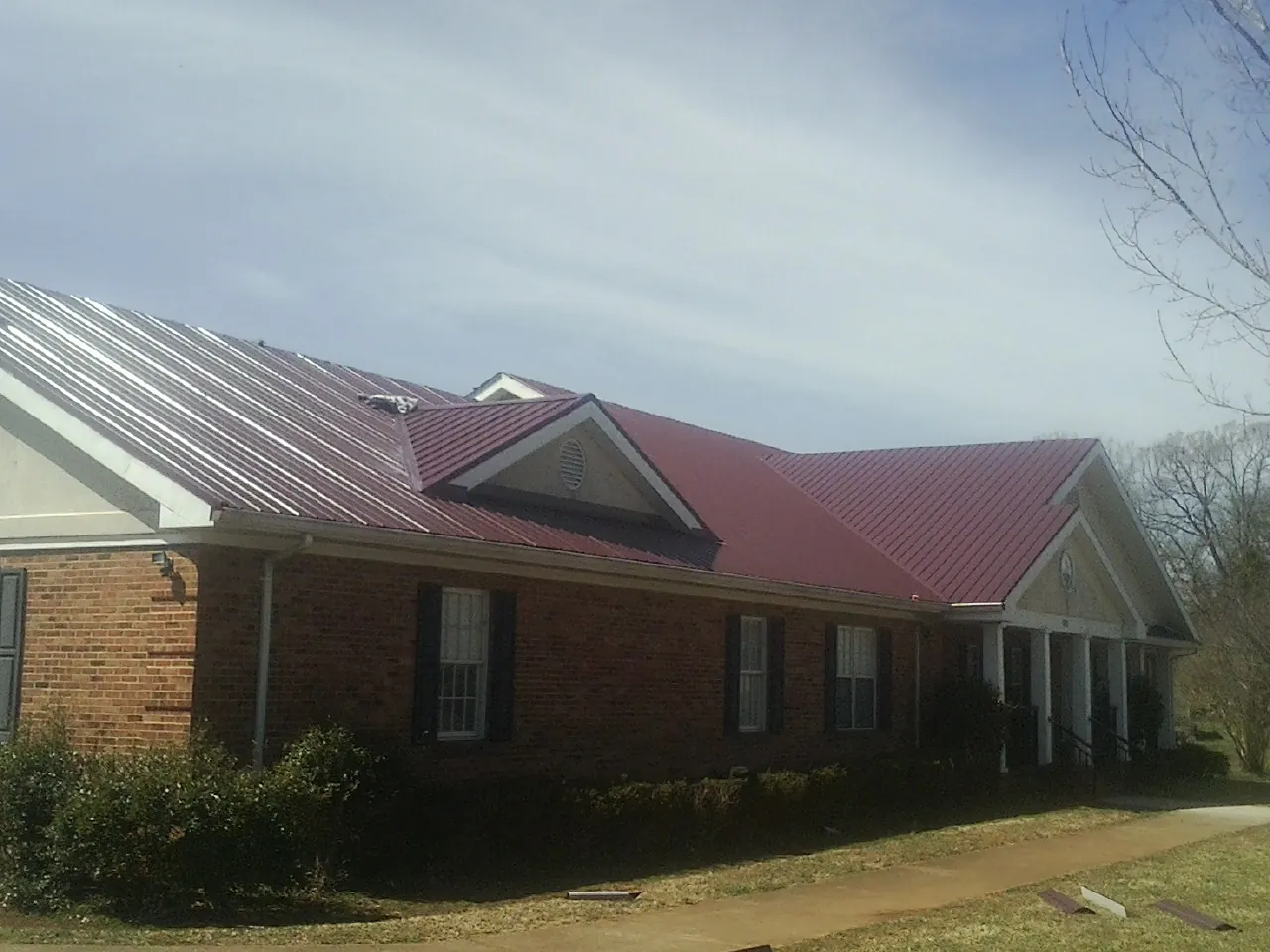 Red metal roof with gabled entries on a long brick building, from a Hail Damage Roof Repair job in West Greenwich