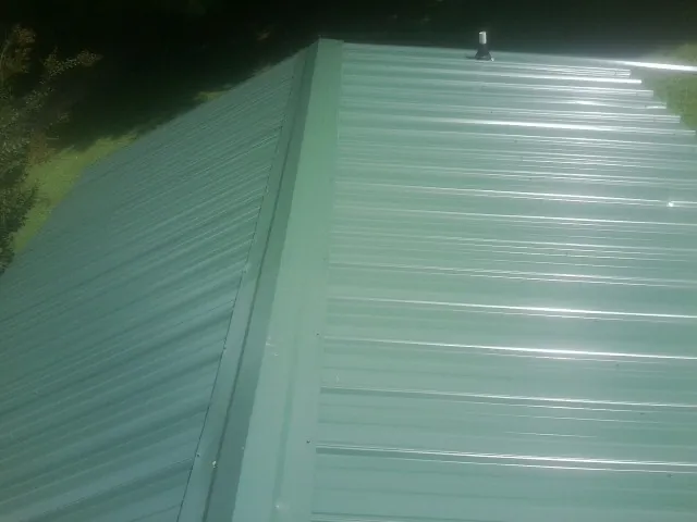 New green metal panels meeting at the ridge of a roof — Flat Roof Repair work by our crew in West Greenwich