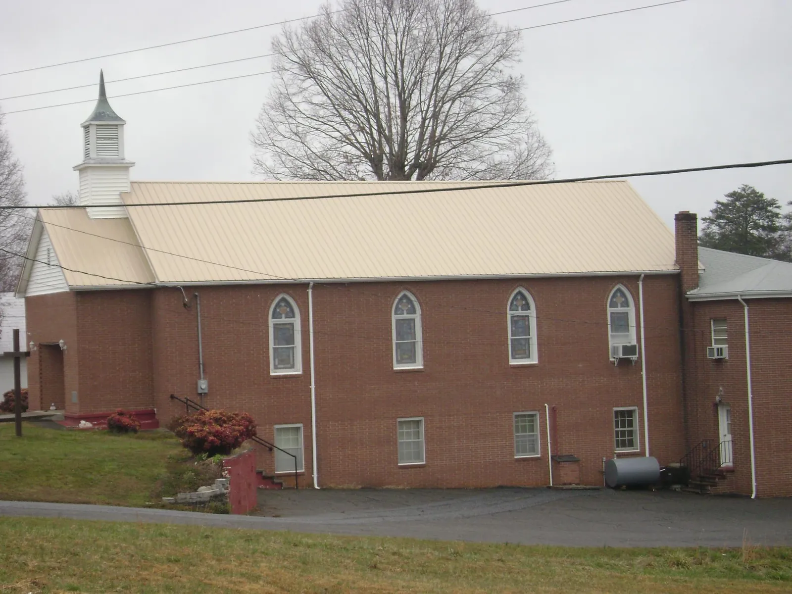 New tan metal roof on a brick church with a white steeple in West Greenwich