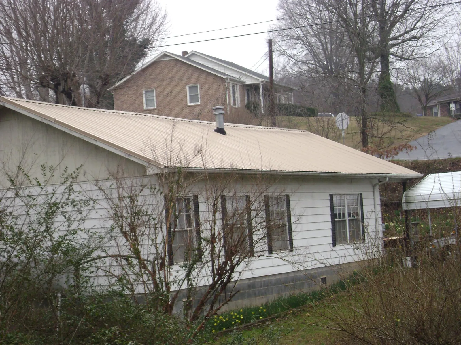 Tan metal roof on a white sided house set into a hillside — Commercial Roofing by Roofing Brothers in West Greenwich